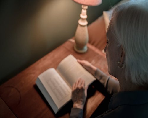 Person reading a physical book with a cozy reading lamp at night